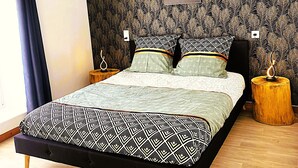 A modern bedroom with a large bed, a wooden floor, and a peacock feather wallpaper. - L'instant d'un souvenir Gite 10 people 135 m² - 4 bedrooms - 7 beds - 2 bathrooms (Taupont)