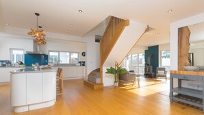 A spacious kitchen with a central island, a wooden staircase, and a modern pendant light. - Solstice, Carbis Bay – Sleeps 8 – Sea Views – Luxury Hot Tub – On-Site Parking (Carbis Bay)