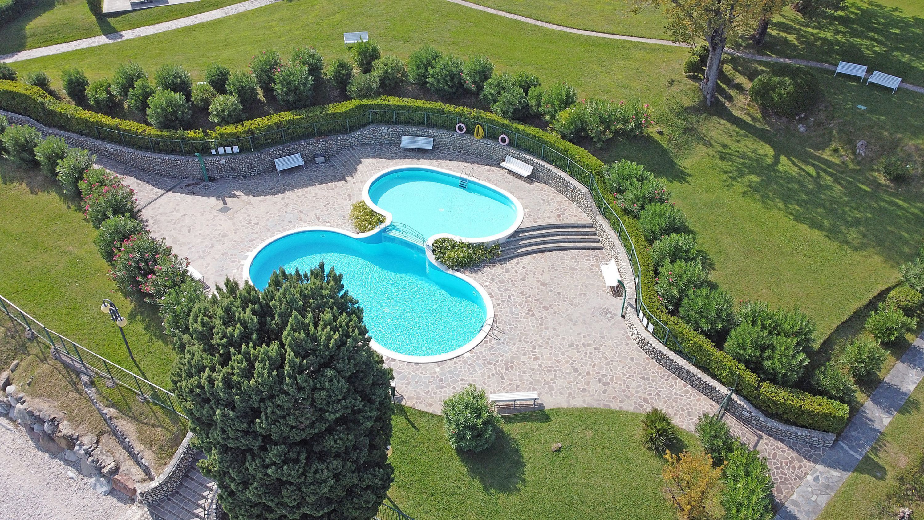 An aerial view of a property with two swimming pools, surrounded by well-maintained lawns and hedges.