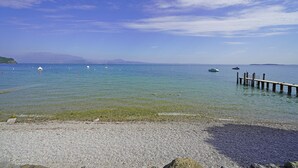 A pebbled beach with clear water and a wooden pier extending into the sea. - Specchio sul Lago in Manerba del Garda (Manerba del Garda)