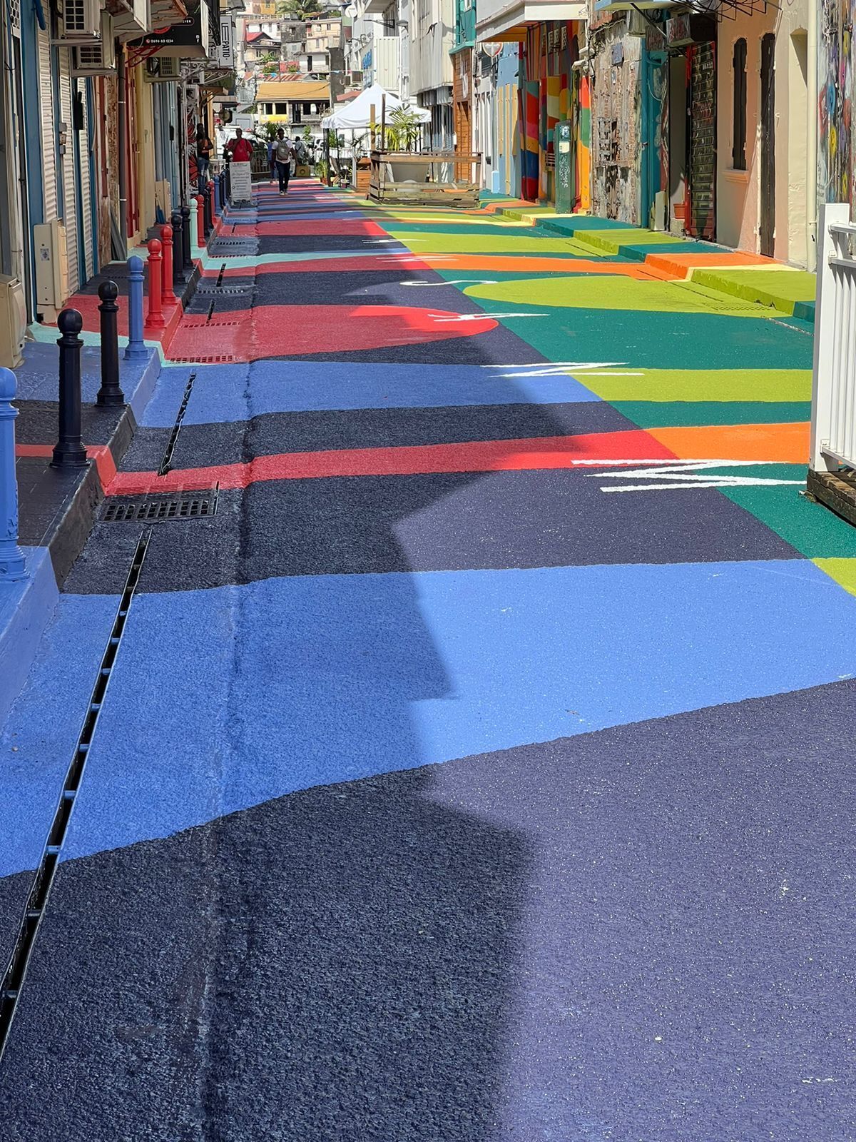 Un passage piéton coloré, équipé d’une grille d’évacuation et de bornes sur le trottoir.