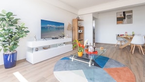 A modern living room with a large flat-screen TV, a glass coffee table, and a dining area with a wooden table and chairs. - Sky Suite in the Heart of the City (Fort-de-France)