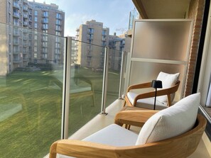 A balcony with two wooden chairs and a small table, overlooking a grassy area and apartment buildings. - Apartment in Nieuwpoort With Terrace (Nieuwpoort)