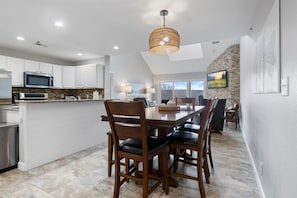 Una cocina moderna con armarios blancos, un microondas y un comedor con una mesa y sillas de madera.