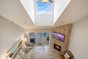 A modern living room with a fireplace, a mounted TV, and a skylight.