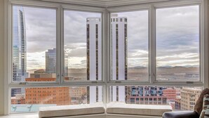 Une chambre d’angle dotée d’une grande fenêtre donnant sur un paysage urbain avec de hauts immeubles et des montagnes.