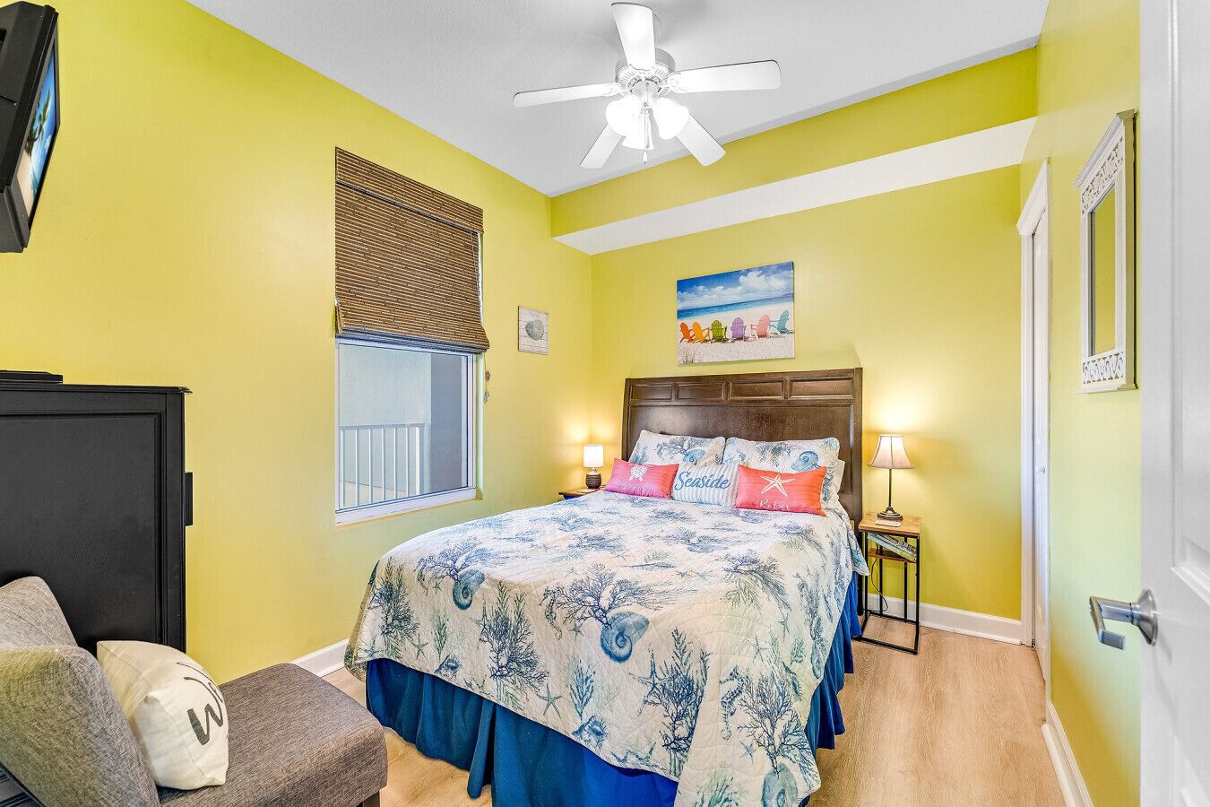 Une chambre à coucher comprenant un lit, des lampes de chevet, un ventilateur de plafond, une fenêtre avec des stores et une porte.