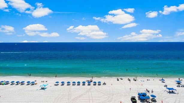 Ein Strand mit blauen Sonnenschirmen und Liegestühlen, ein klarer, blauer Himmel und das Meer.
