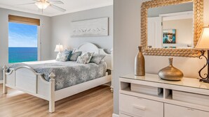 Ein Schlafzimmer mit einem Bett, einem Deckenventilator, einem Fenster mit Meerblick und einem Nachttisch mit Lampe und einer Vase.