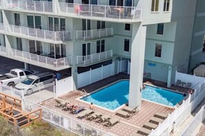 Ein mehrgeschossiges Gebäude mit einem zentralen Schwimmbecken, umgeben von Liegestühlen und einem eingezäunten Deck.