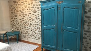 A room with a stone wall, a teal cabinet, a small round table, and a patterned rug. - Vercors en vert (Saint-Romans)