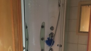 A glass-enclosed shower with a handheld showerhead, a built-in seat, and a small shelf with toiletries. - Vercors en vert (Saint-Romans)