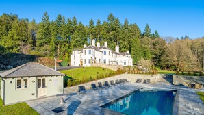 Une grande maison avec une piscine, entourée d’une pelouse bien entretenue et d’arbres.