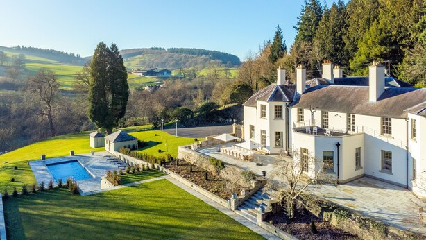 Un grand bâtiment blanc doté d’une piscine, entouré d’une pelouse bien entretenue et offrant une vue sur des collines ondulantes.