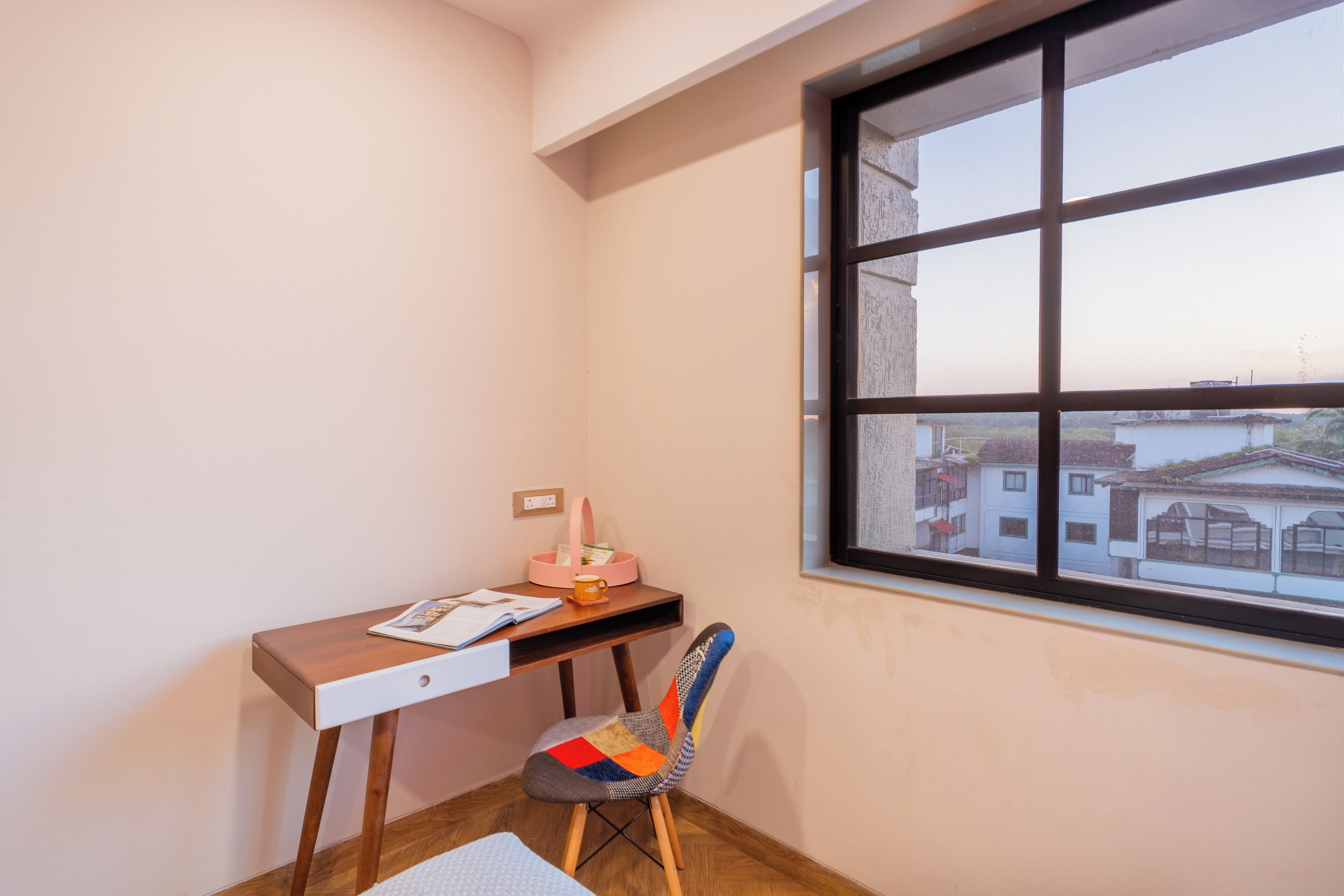 A corner room with a desk, chair, and a window with a view of buildings.