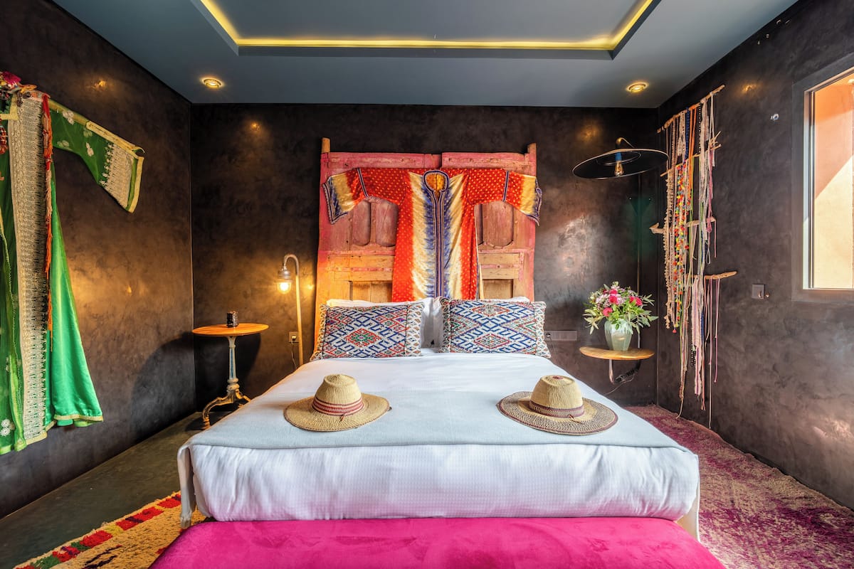 A modern bedroom with a large bed, decorative pillows, a bedside table, and a hanging plant.