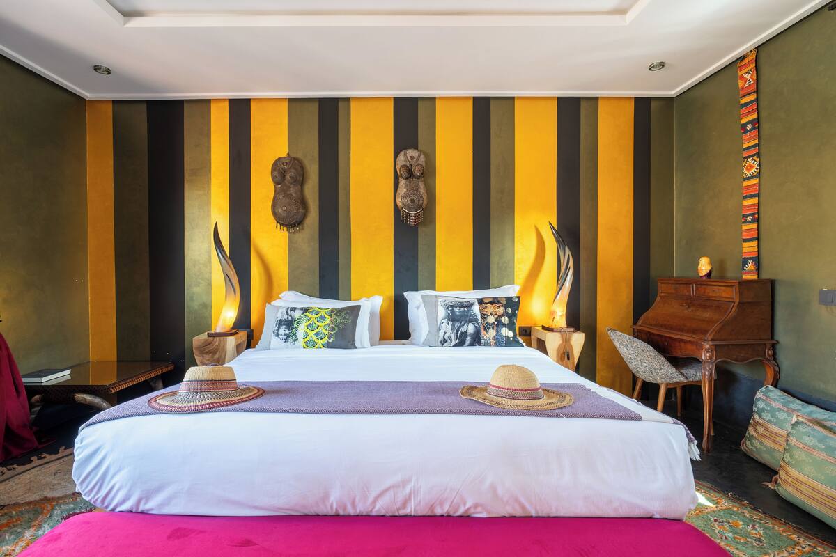 A hotel room with a bed, two nightstands, a wooden desk, a chair, and a sofa.