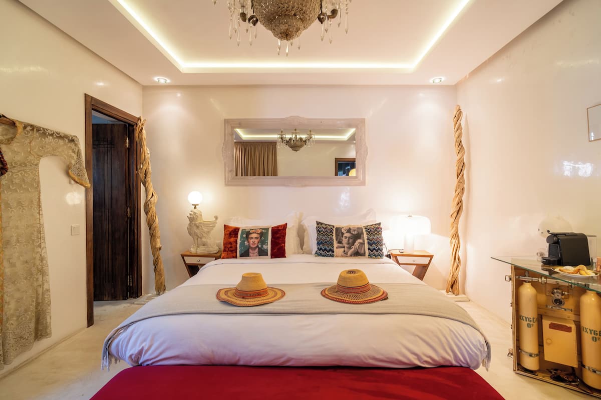 A well-lit bedroom with a large bed, a mirror, and a bedside table with a lamp.