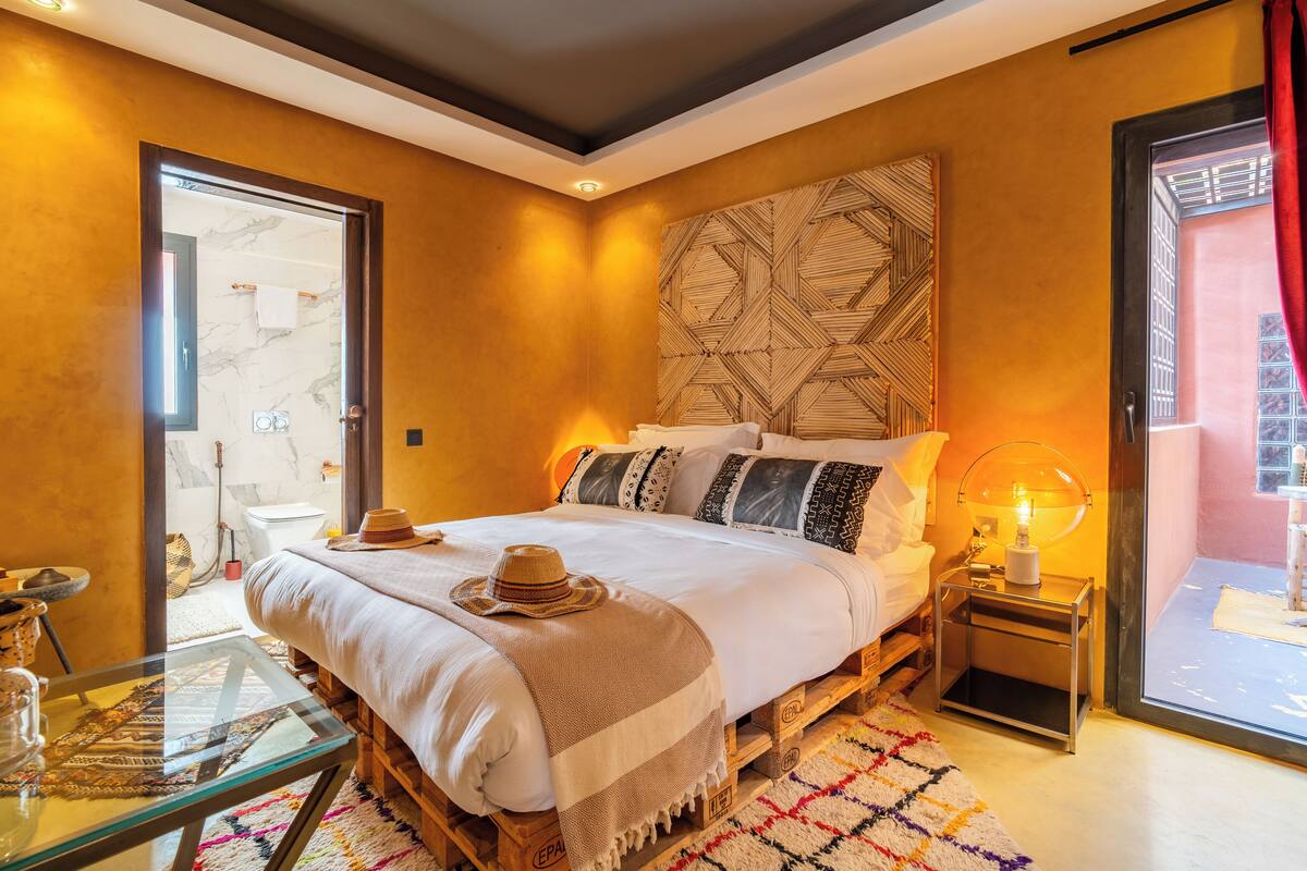 A cozy bedroom with a bed, a nightstand, a glass table, and a view of the outside.