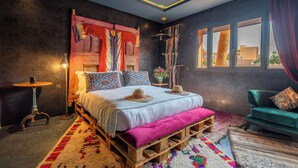A bedroom with a bed, a bench, a chair, a table, and a window with curtains. - Villa Otia (Marrakech)