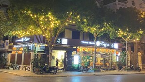A street with two coffee shops, outdoor seating, and trees with string lights. - AMY HOTEL (Kinh Bac)