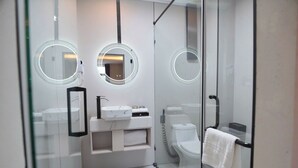 A modern bathroom with a glass shower enclosure, a white sink with a black faucet, and two round mirrors with lighted frames. - AMY HOTEL (Kinh Bac)