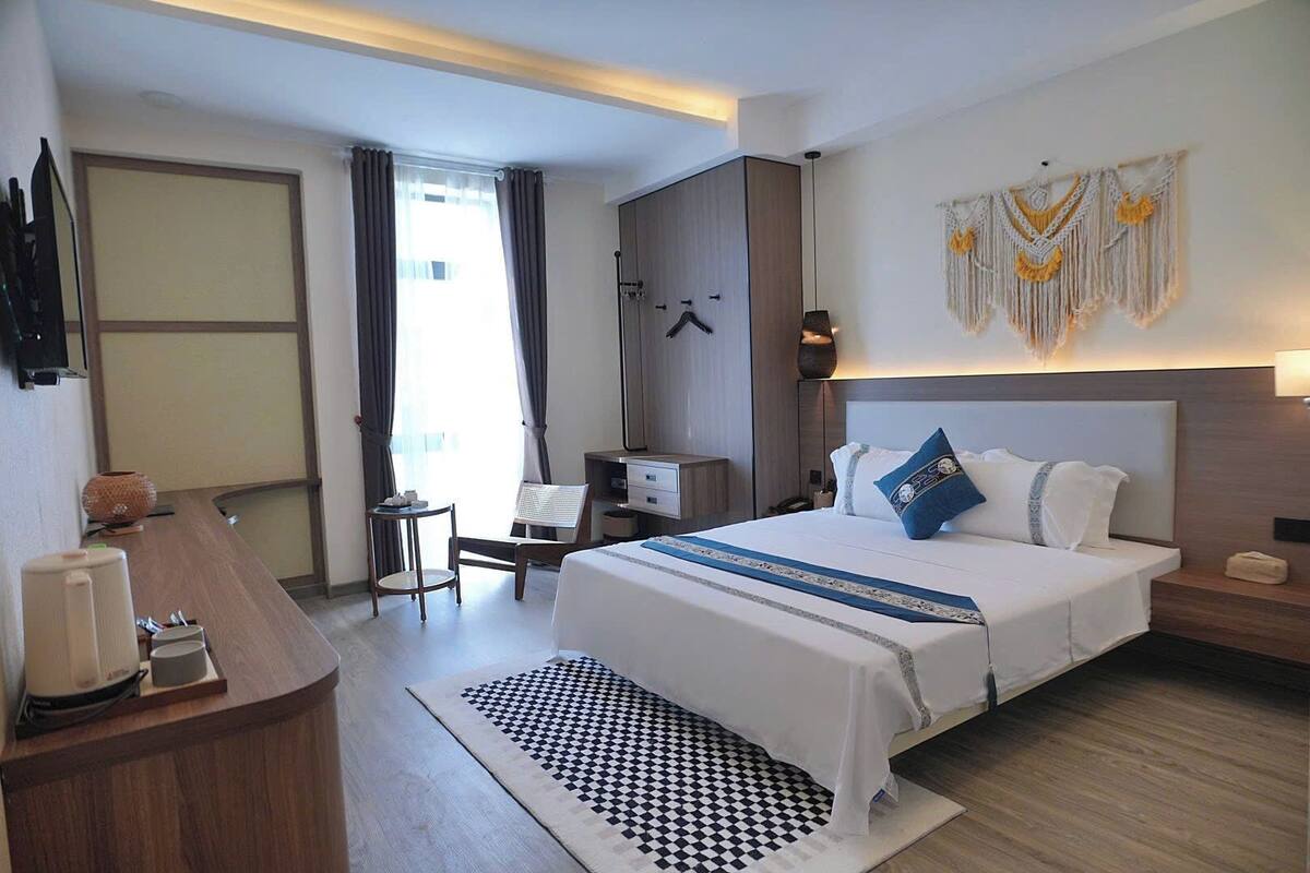 Una habitación de hotel con una cama grande, un escritorio, una silla, un armario y una lámpara de pared.