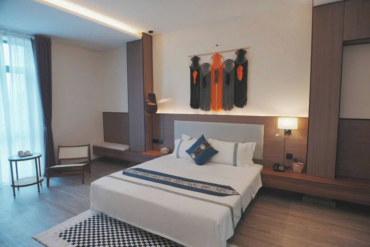 Habitación de hotel con una cama grande, una mesita de noche, una lámpara y un tapiz decorativo.