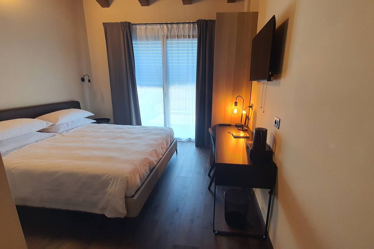 A hotel room with a bed, a desk with a lamp, and a TV mounted on the wall.