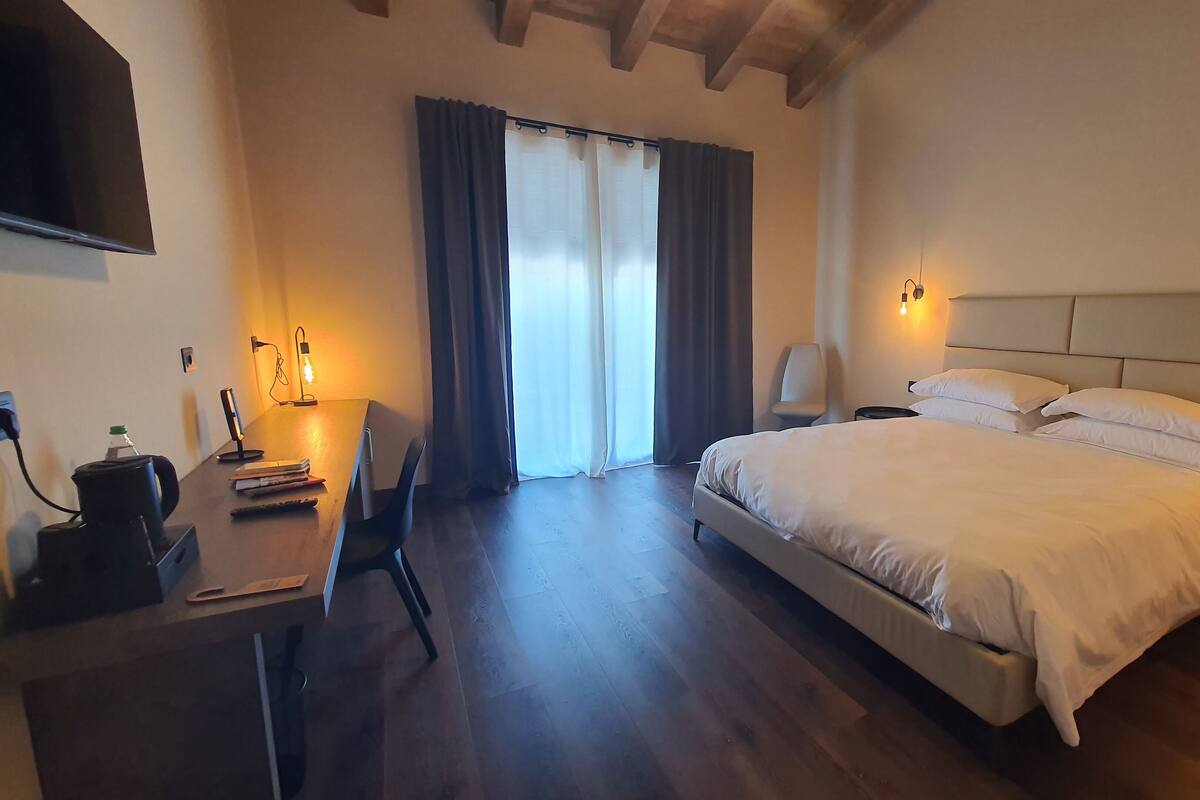 A hotel room with a bed, a desk with a chair, a coffee maker, and a TV mounted on the wall.