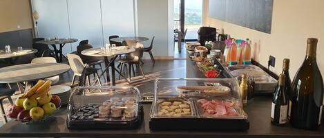 A buffet setup with various food items and beverages, including fruits, meats, and bottles.