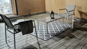 A balcony with a glass table, two chairs, a patterned rug, and a lantern.