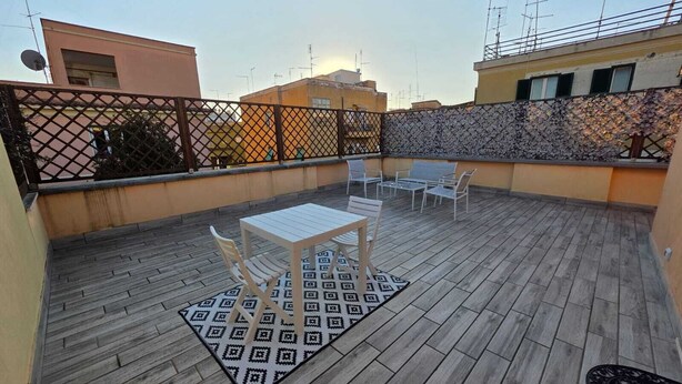 A rooftop patio with a table and chairs, a patterned rug, and a stone wall.