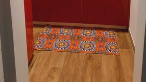 A compact kitchen with red cabinets, a stainless steel sink, and a patterned rug.