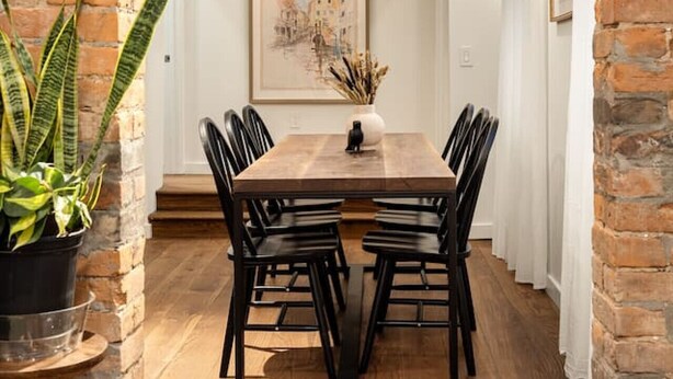 Een eetruimte met een houten tafel en zwarte stoelen, bakstenen muren en een hanglamp.