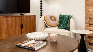 Een woonkamer met een televisie, een lamp, een schilderij, een bank, een salontafel en een boek.
