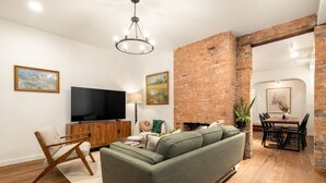 Een moderne woonkamer met een groene bank, houten vloer, bakstenen muur en een eethoek met een tafel en stoelen.