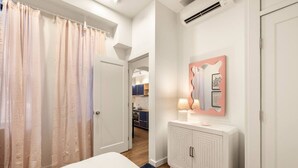 Een slaapkamer met een bed, een witte kast, een spiegel met kunstwerk, en een badkamer zichtbaar door een open deur.