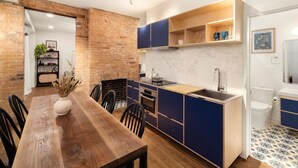 Een moderne keuken met blauwe kastjes, een houten eettafel en een bakstenen muur.