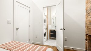 A bedroom with a bed, a bathroom with a washing machine, and a brick wall.