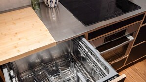 A kitchen with a dishwasher, a wooden cutting board, and a black induction cooktop.