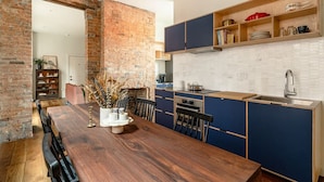Een moderne keuken met een houten eettafel, blauwe keukenkastjes en een bakstenen muur.