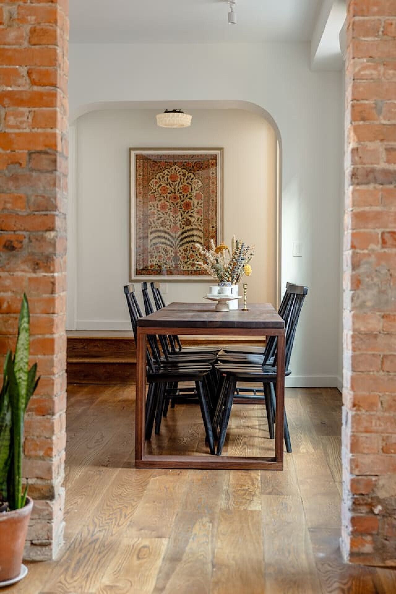 Uma área de refeições com uma mesa e cadeiras de madeira, uma planta em vaso e um objeto decorativo grande na parede.