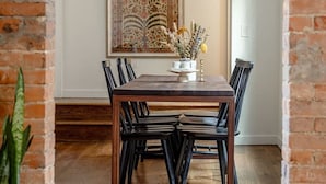 Een eetgedeelte met een houten tafel en stoelen, een potplant en een groot decoratief object aan de muur.