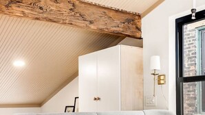 A bedroom with a bed, a wooden ceiling, a window, and a white wardrobe.