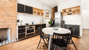 A modern kitchen with a brick wall, wooden shelves, and a dining area with a round table and chairs.