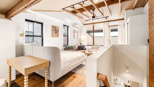 A loft-style room with exposed wooden beams, a loft bed, a small table, and a sofa.