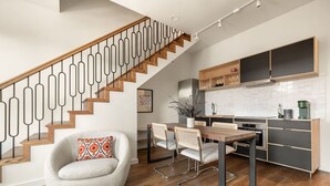 A modern kitchen with wooden cabinets, a dining area with a wooden table and chairs, and a staircase with a unique railing design.