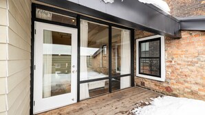 A modern building with large glass doors, a wooden deck, and a brick wall.