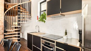 Une cuisine moderne avec un escalier en colimaçon en bois, des meubles noirs et des appareils électroménagers en acier inoxydable.
